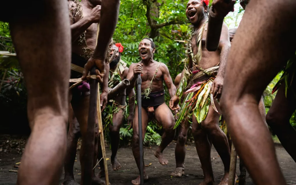 Menschen mit Pflanzenschmuck versammeln sich unter Bäumen in Vanuatu.